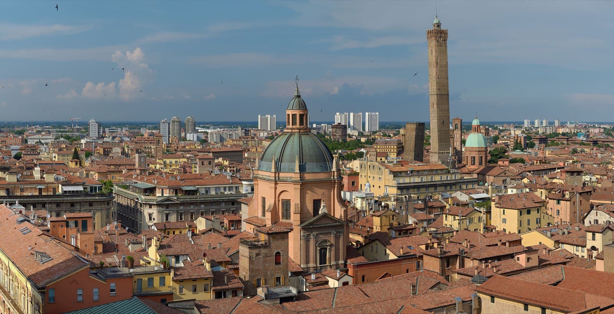 Acoperișurile roșii ale Bolognei văzute de pe San Petronio, cu domul sanctuarului Santa Maria della Vita în prim-plan și Turnul Asinelli în dreapta.