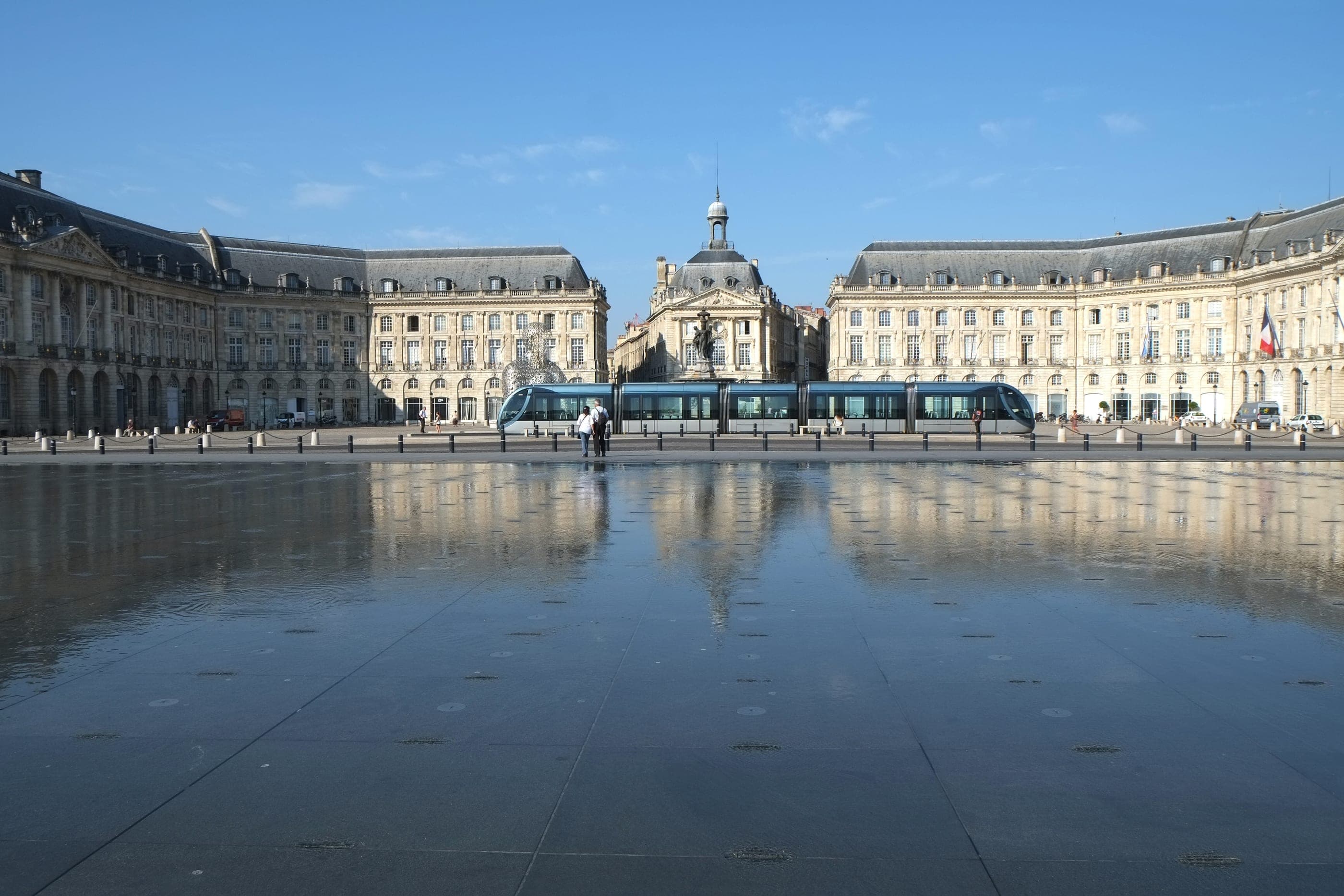 Place de la Bourse oglindită în Miroir d'eau, cu un tramvai trecând pe chei.