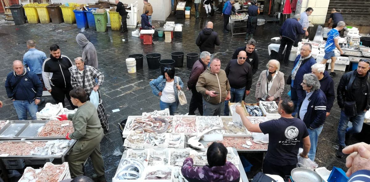 Tarabe cu pește și cumpărători în piața La Pescheria din Catania.