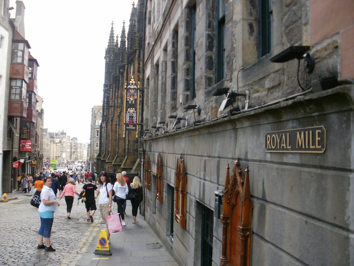 Royal Mile din Edinburgh, cu placa străzii pe zid și un turn gotic în fundal.
