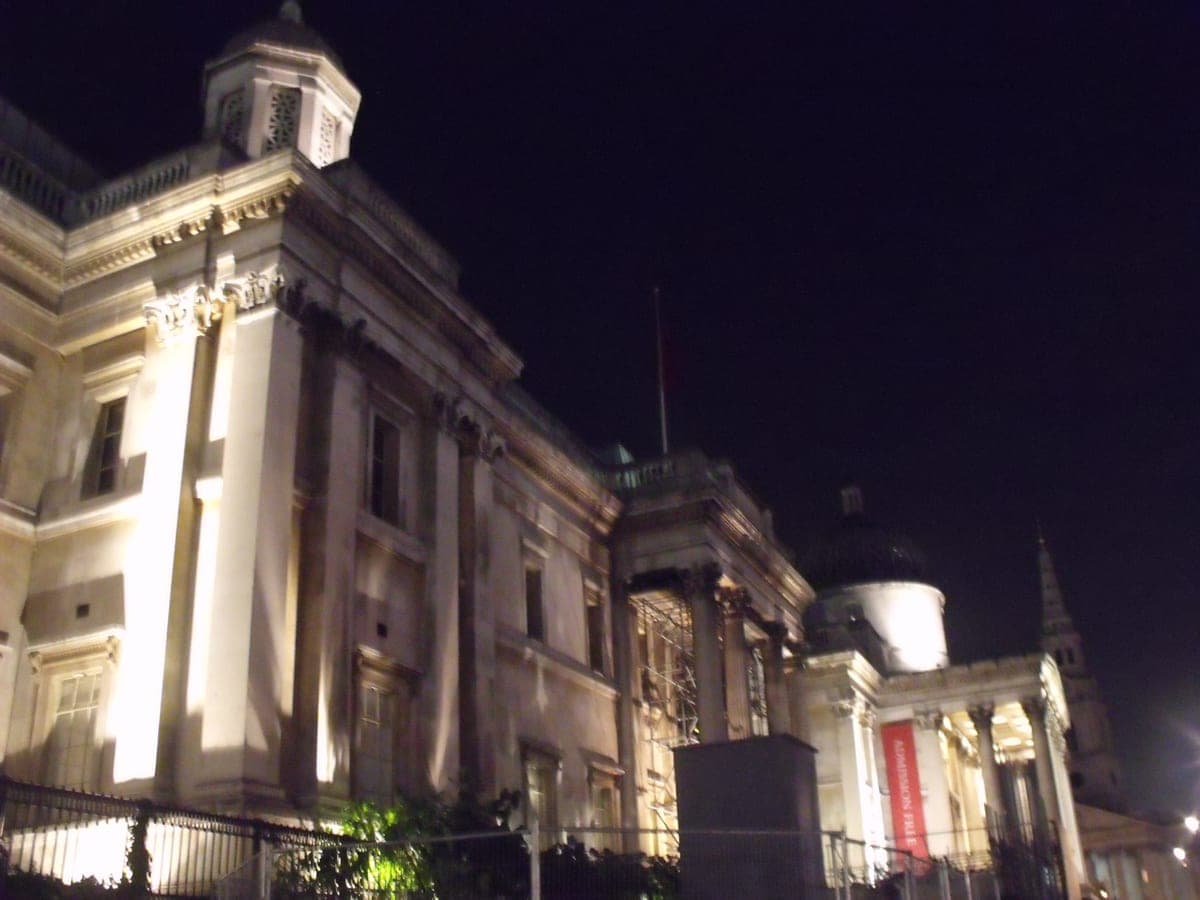 Faţada National Gallery din Trafalgar Square, luminată noaptea, cu banerul „Admission free".