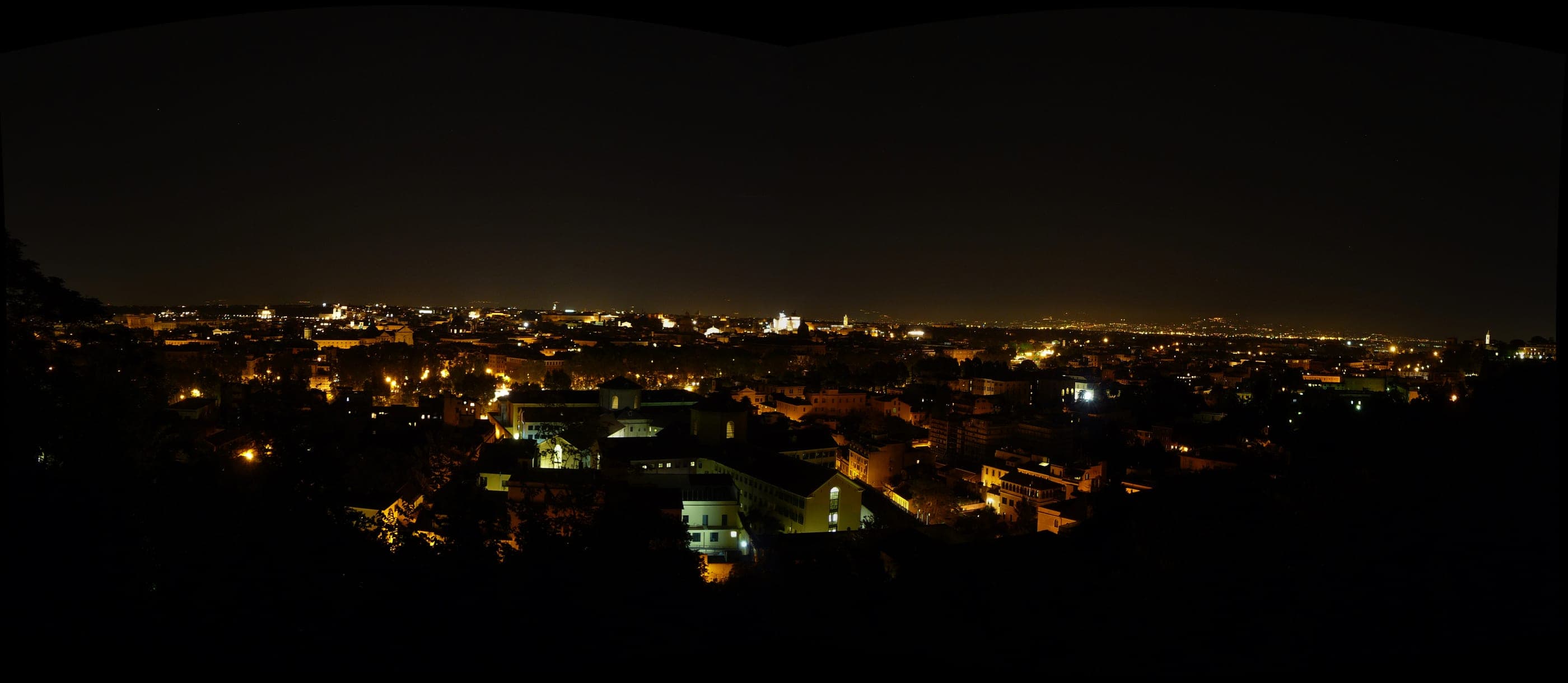 Roma noaptea, văzută de pe dealul Gianicolo, cu cupolele luminate peste acoperişuri.