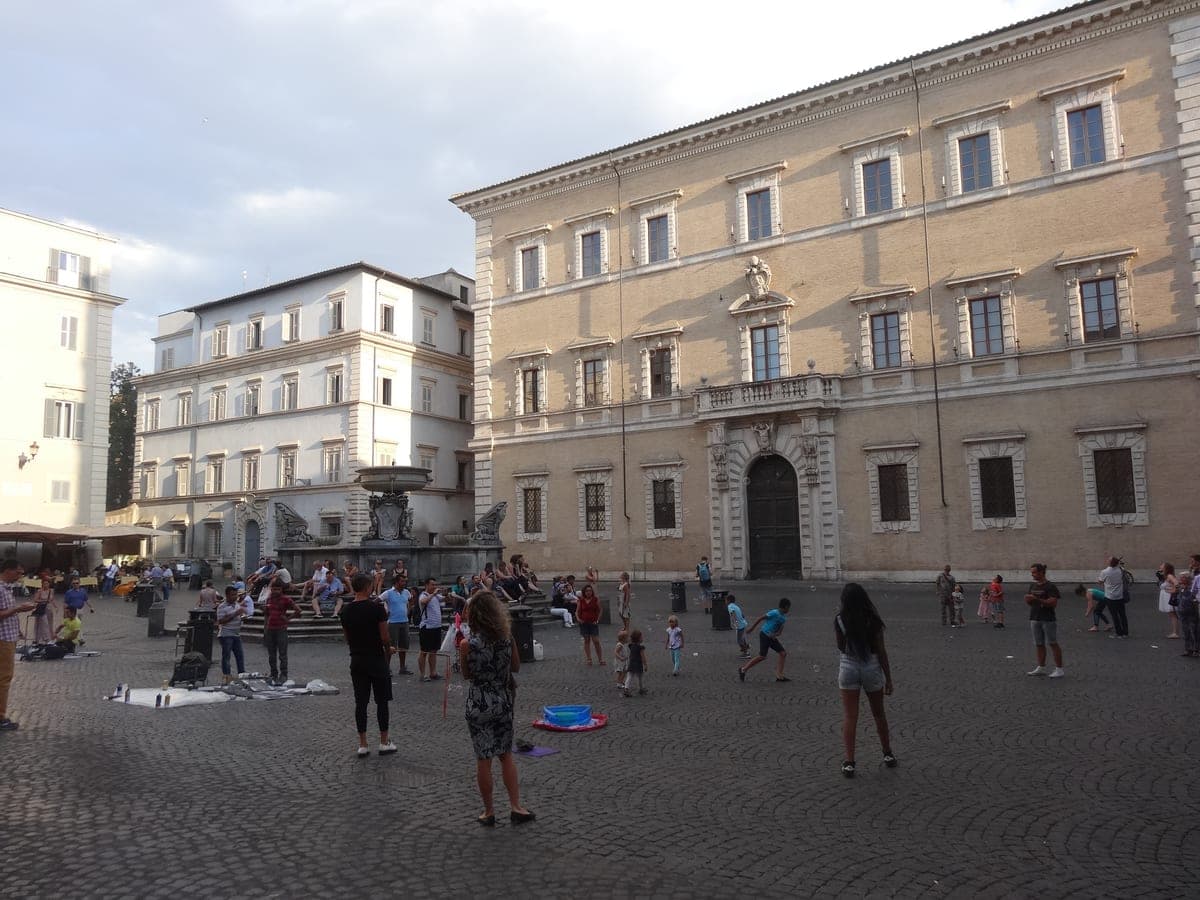 Piazza di Santa Maria in Trastevere, cu fântâna și oameni pe pavaj, între casele vechi.