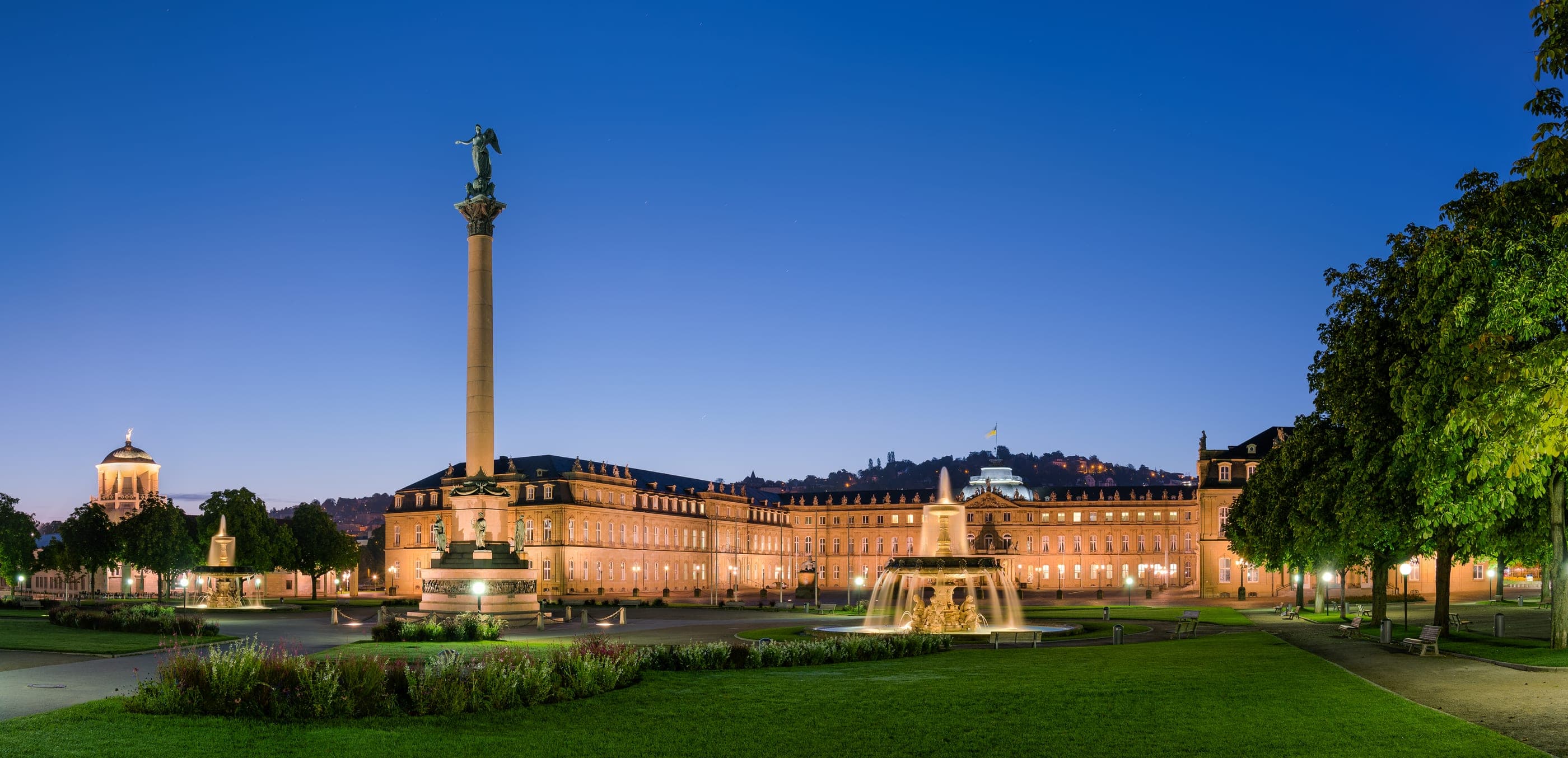 Schlossplatz la căderea serii, cu Jubiläumssäule, fântâna și Neues Schloss în spate.