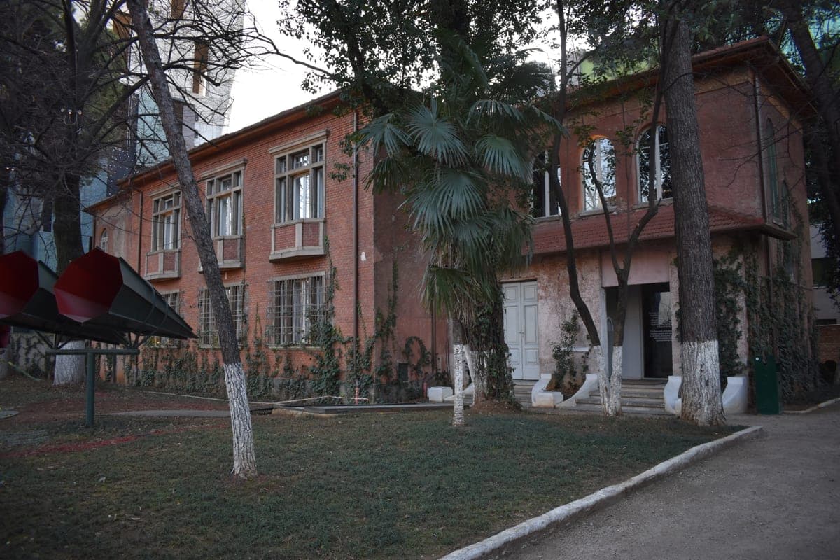 Clădirea roz a muzeului Shtëpia me Gjethe din Tirana, între copaci.