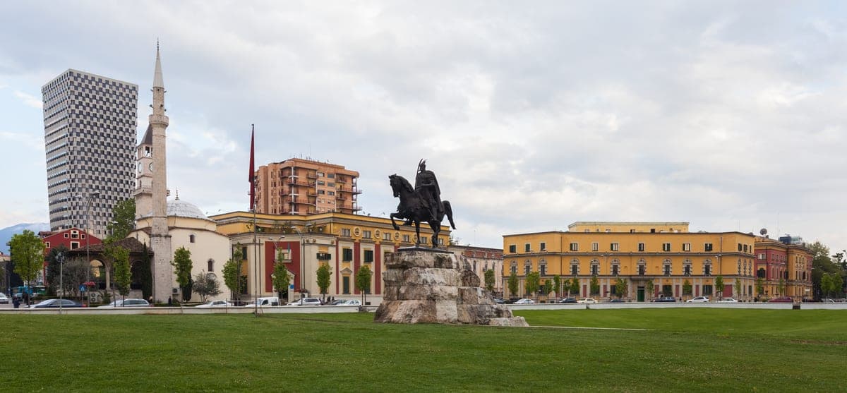 Statuia lui Skanderbeg în piața centrală a Tiranei, cu moscheea și clădirile galbene în spate.